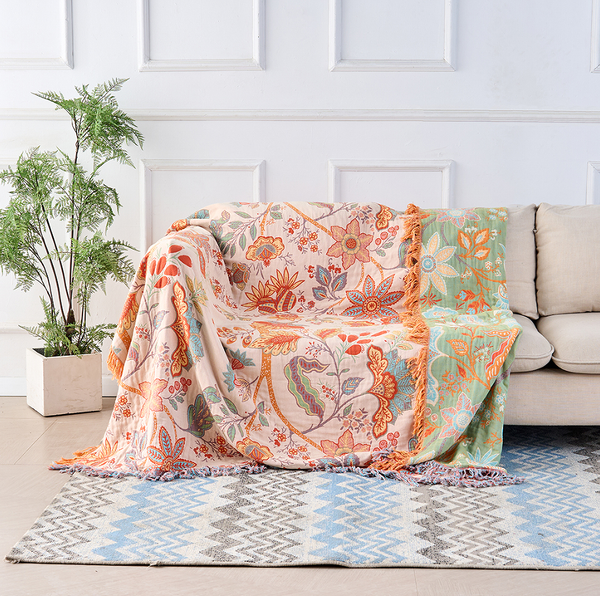 Boho floral cotton throw blanket in cream with orange and blue tapestry print draped over a sofa